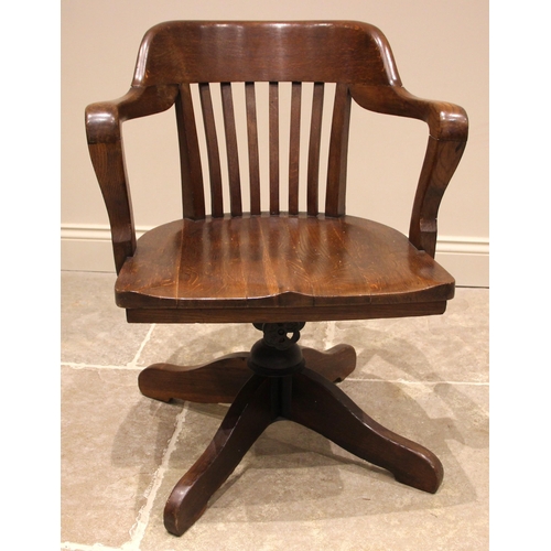 1037 - An early 20th century oak office/desk chair, the concave lath back extending to down swept arms over... 