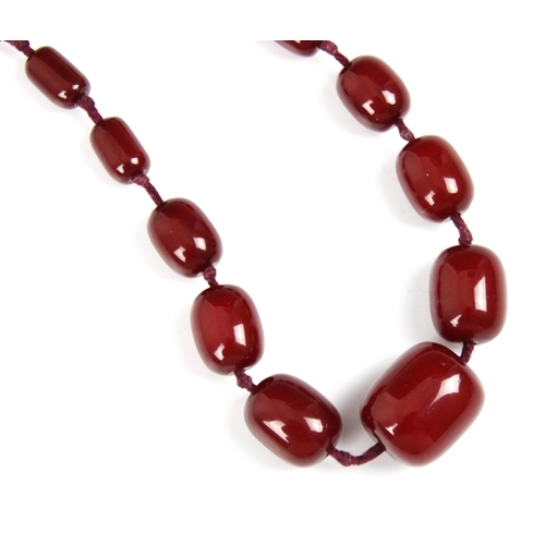 158 - A string of cherry coloured 'amber' beads, the graduated barrel shaped beads strung upon red string,... 