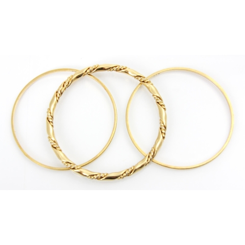 174 - A pair of yellow metal bangles, with applied grooved detail, each engraved ‘22k’ 18gms, with a furth... 