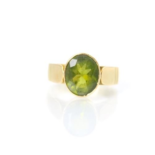 188 - A 20th century peridot ring, the oval cut peridot within yellow metal rubover mount, leading to wide... 