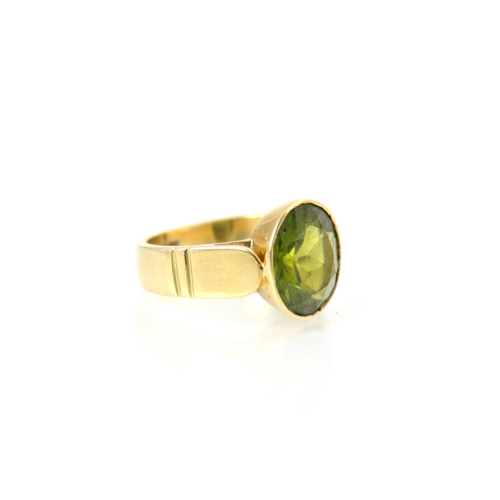 188 - A 20th century peridot ring, the oval cut peridot within yellow metal rubover mount, leading to wide... 