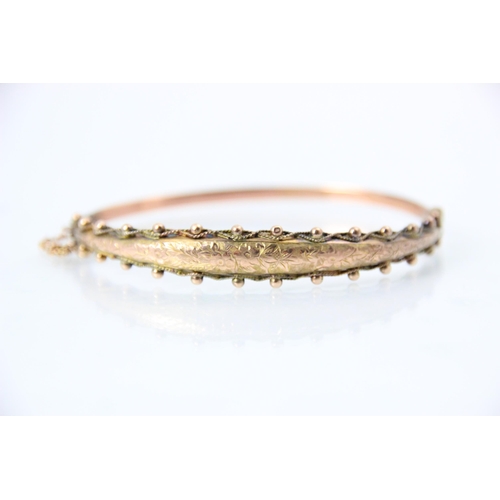 226 - An early 20th century 9ct rose gold bangle, the raised engraved front with spherical and beaded deta... 