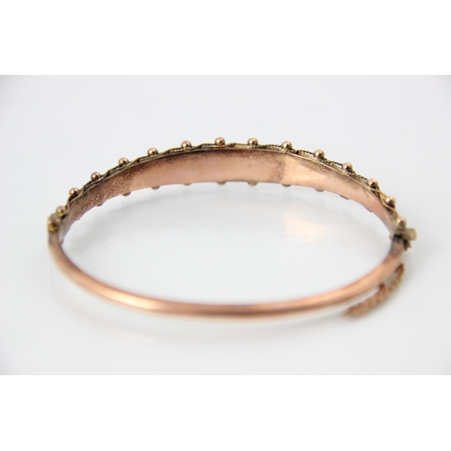 226 - An early 20th century 9ct rose gold bangle, the raised engraved front with spherical and beaded deta... 