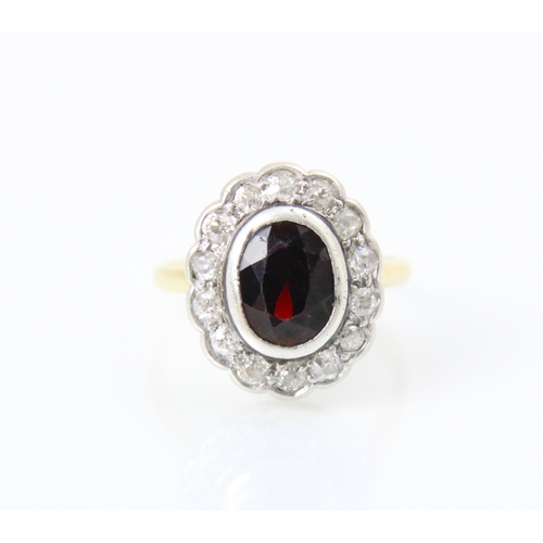 259 - A 20th century garnet and diamond cluster ring, the oval cut red stone with a surround of fourteen m... 