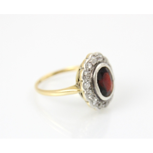 259 - A 20th century garnet and diamond cluster ring, the oval cut red stone with a surround of fourteen m... 