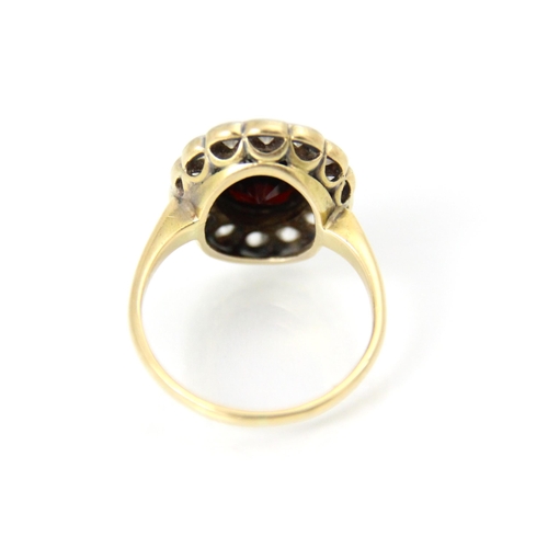 259 - A 20th century garnet and diamond cluster ring, the oval cut red stone with a surround of fourteen m... 