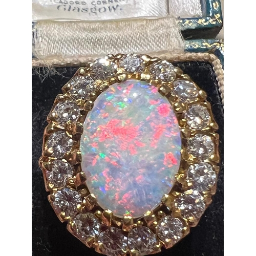 308 - An opal and diamond cluster ring, the large precious opal oval cabochon claw set with a surround of ... 