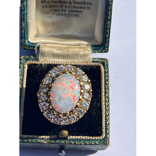 308 - An opal and diamond cluster ring, the large precious opal oval cabochon claw set with a surround of ... 