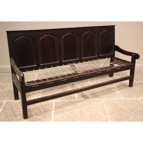 944 - A George III oak panel back settle, the five fielded panels extending to down swept arms upon legs o... 