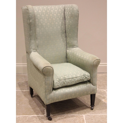 946 - A George III style wingback fireside armchair, late 19th/early 20th century, upholstered in a green ... 