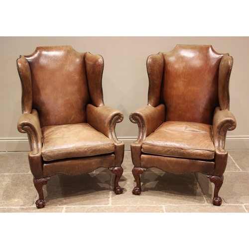 947 - A pair of George III style tan leather wingback armchairs, late 20th century, each with a shaped bac... 