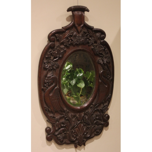 876 - A carved oak wall mirror, late 19th century, the central oval mirror plate within a frame carved in ... 