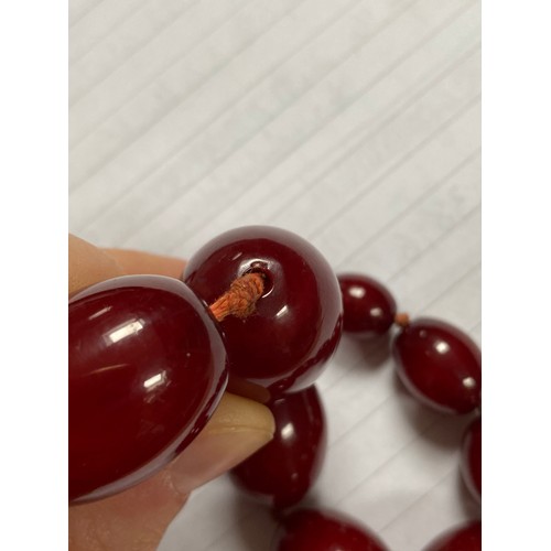 160 - A string of cherry coloured 'amber' beads, the graduated oval beads strung upon string, largest bead... 