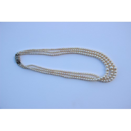 283 - A triple strand of pearls, the graduated pearls of non uniform form, upon an associated marcasite se... 