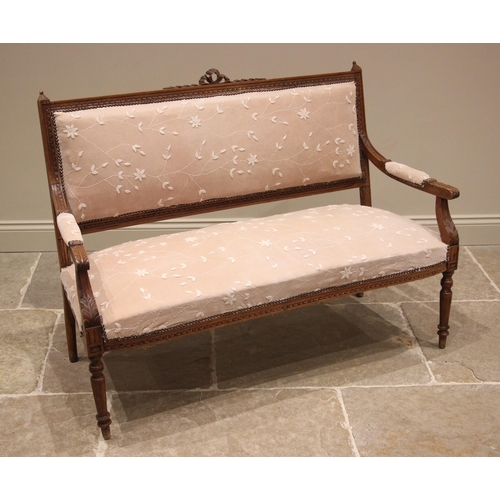 1041 - An Edwardian walnut framed sofa, the padded back rest centred with a ribbon tied crest, extending to... 