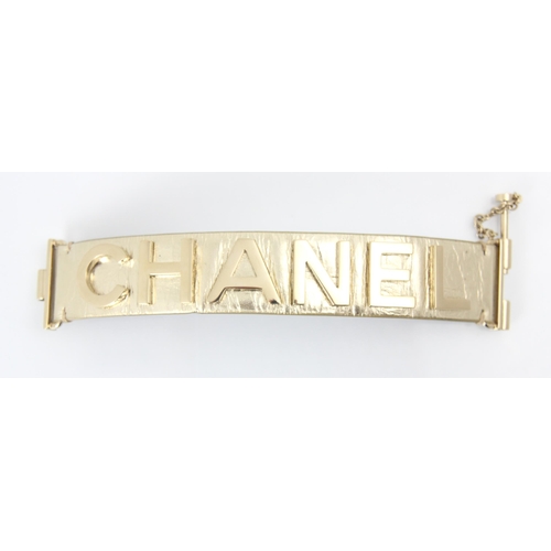 262 - A Chanel leather bracelet, the light gold toned cuff with applied CHANEL lettering, with slide lock ... 