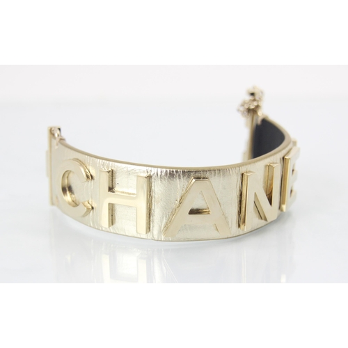 262 - A Chanel leather bracelet, the light gold toned cuff with applied CHANEL lettering, with slide lock ... 