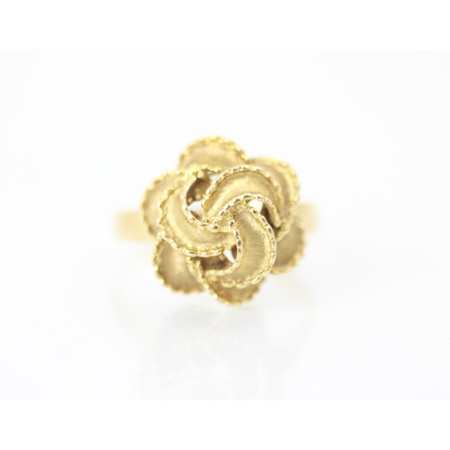 266 - A yellow metal dress ring, the knot designed head with matte and polished frilled detail, set to pla... 