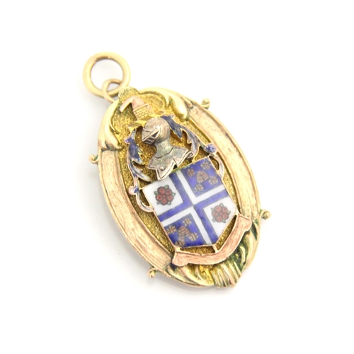 128 - A yellow metal pendant, the oval pendant with applied enamel shield motif surmounted by a knight, wi... 