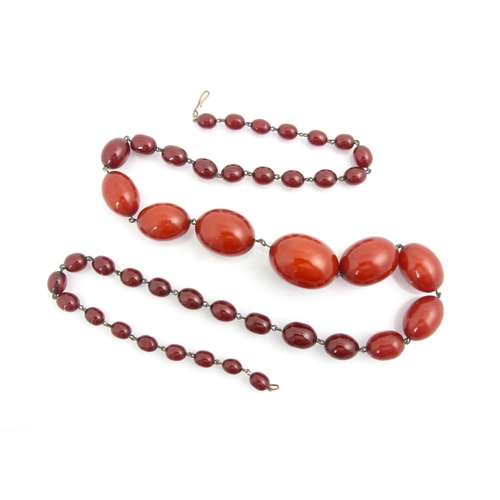 79 - A string of cherry coloured 'amber' beads, the forty two graduated polished oval beads with base met... 