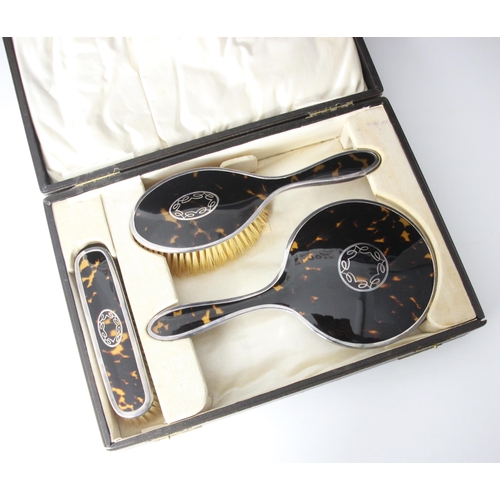38 - A cased George V silver and tortoiseshell mounted dressing table set, comprising hand held mirror, c... 