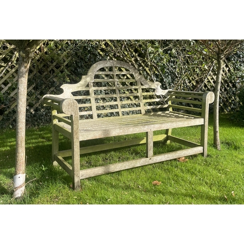 866 - A Lutyens hardwood slatted garden bench, of typical construction, with an arched back rest upon legs... 