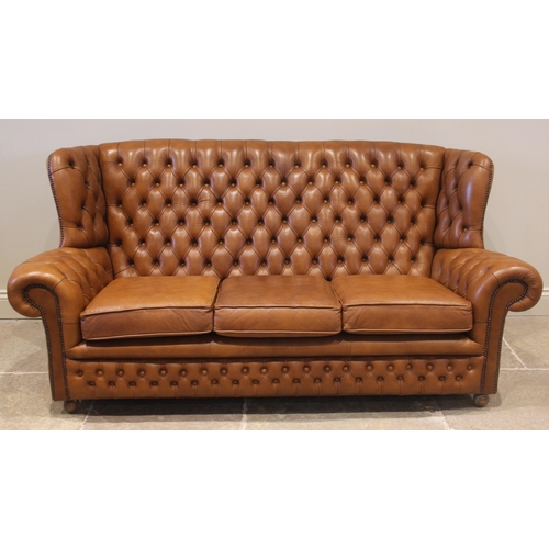 858 - A tan leather wing back sofa and conforming armchair, both with a button back extending to shaped wi... 