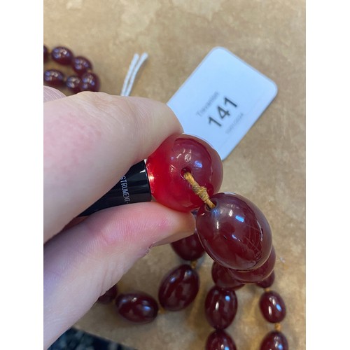 141 - A string of cherry coloured 'amber' beads, the fifty two graduated barrel shaped beads upon string, ... 
