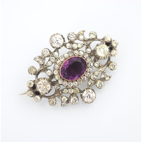 197 - An early 20th century brooch, the central purple oval paste stone within openwork sinuous design wit... 