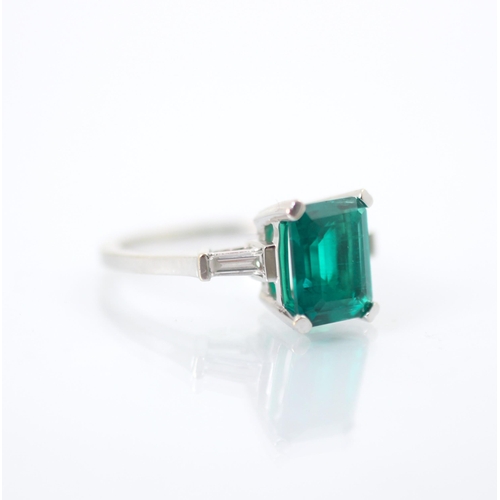 244 - A synthetic emerald and diamond set ring, the emerald cut synthetic emerald set with white metal cla... 