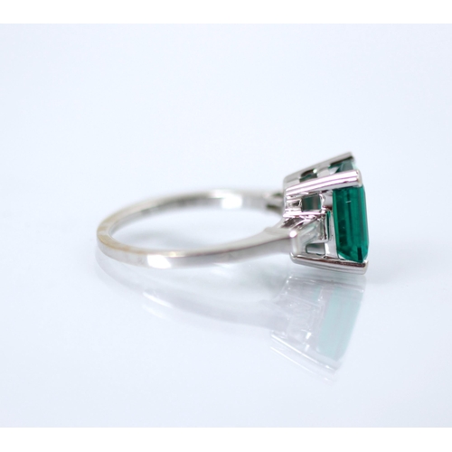 244 - A synthetic emerald and diamond set ring, the emerald cut synthetic emerald set with white metal cla... 