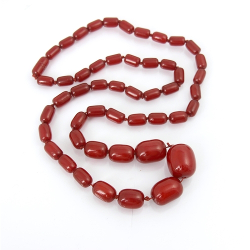 258 - A string of cherry coloured ‘amber’ beads, fifty graduated barrel shaped beads, overall length 82cm,... 