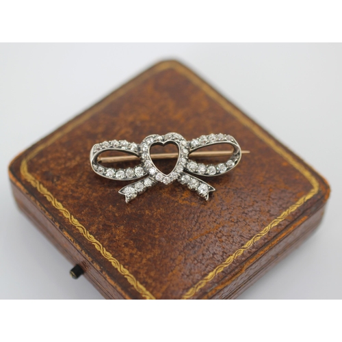 256 - An early 20th century diamond heart brooch, the central heart motif within an openwork bow, set thro... 