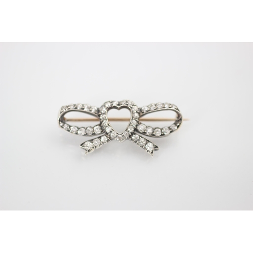 256 - An early 20th century diamond heart brooch, the central heart motif within an openwork bow, set thro... 