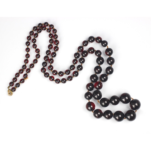 202 - A string of cherry coloured 'amber' beads, the eighty six graduated polished spherical beads with bo... 