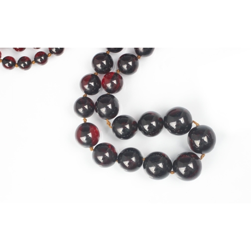 202 - A string of cherry coloured 'amber' beads, the eighty six graduated polished spherical beads with bo... 