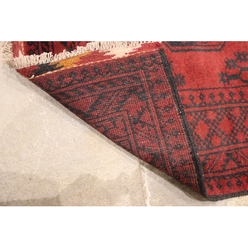 724 - A washed red Afghan double knot rug, full pile Bokhara, the three octagonal medallions upon a red gr... 