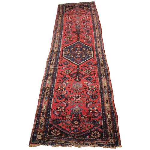 733 - A Caucasian hand knotted wool runner, in red, blue and brown colourways, the central hexagonal blue ... 