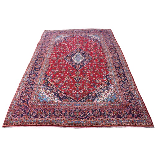 713 - A large red ground Persian Kashan carpet, in red, blue, green and ivory colourways, the central red ... 