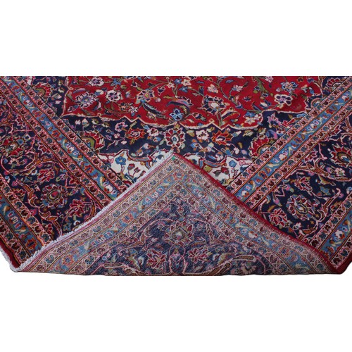 713 - A large red ground Persian Kashan carpet, in red, blue, green and ivory colourways, the central red ... 