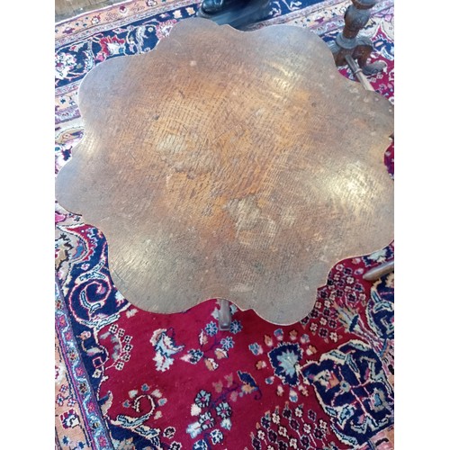 869 - A 19th century oak tripod table, the scalloped circular top upon a baluster column and three shaped ... 