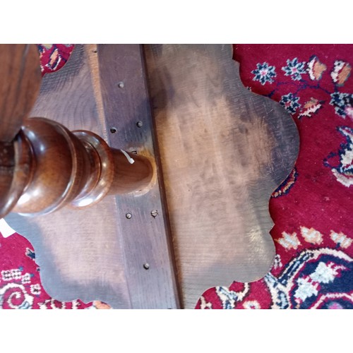 869 - A 19th century oak tripod table, the scalloped circular top upon a baluster column and three shaped ... 