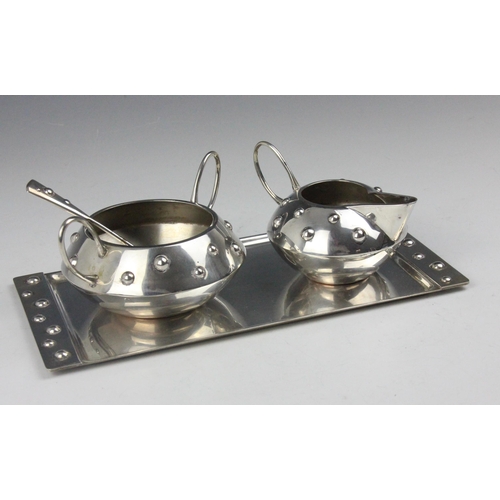 128 - An early 20th century silver coloured Arts and Crafts part tea service, comprising sugar bowl, milk ... 