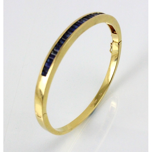 189 - A yellow metal and untested sapphire set bangle, the twenty nine calibre cut sapphires channel set i... 