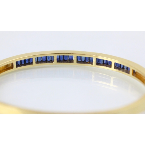 189 - A yellow metal and untested sapphire set bangle, the twenty nine calibre cut sapphires channel set i... 