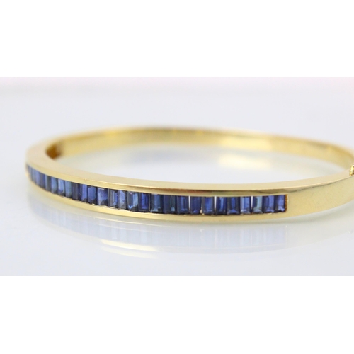 189 - A yellow metal and untested sapphire set bangle, the twenty nine calibre cut sapphires channel set i... 