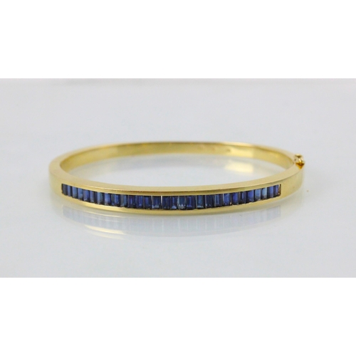 189 - A yellow metal and untested sapphire set bangle, the twenty nine calibre cut sapphires channel set i... 