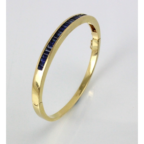 189 - A yellow metal and untested sapphire set bangle, the twenty nine calibre cut sapphires channel set i... 