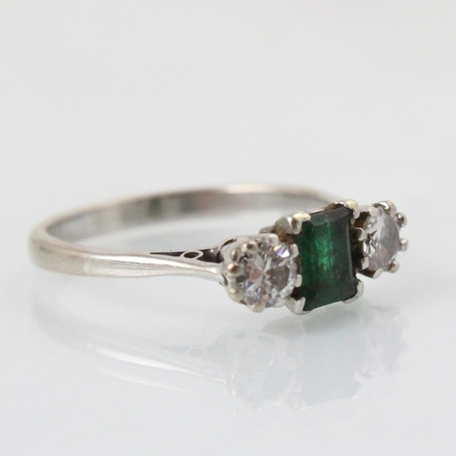 251 - An emerald and diamond three stone ring, the emerald cut stone with a round cut diamond to each side... 