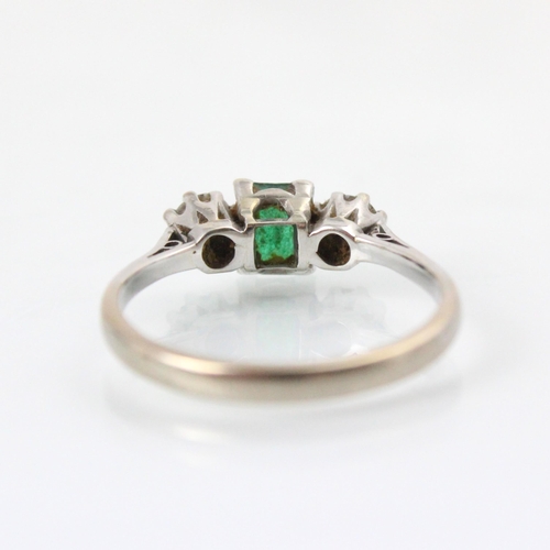 251 - An emerald and diamond three stone ring, the emerald cut stone with a round cut diamond to each side... 